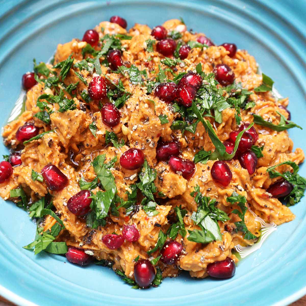 Paprika-Linsen-Aufstrich mit Granatapfelkernen und frischer Petersilie auf einem türkisfarbenen Teller