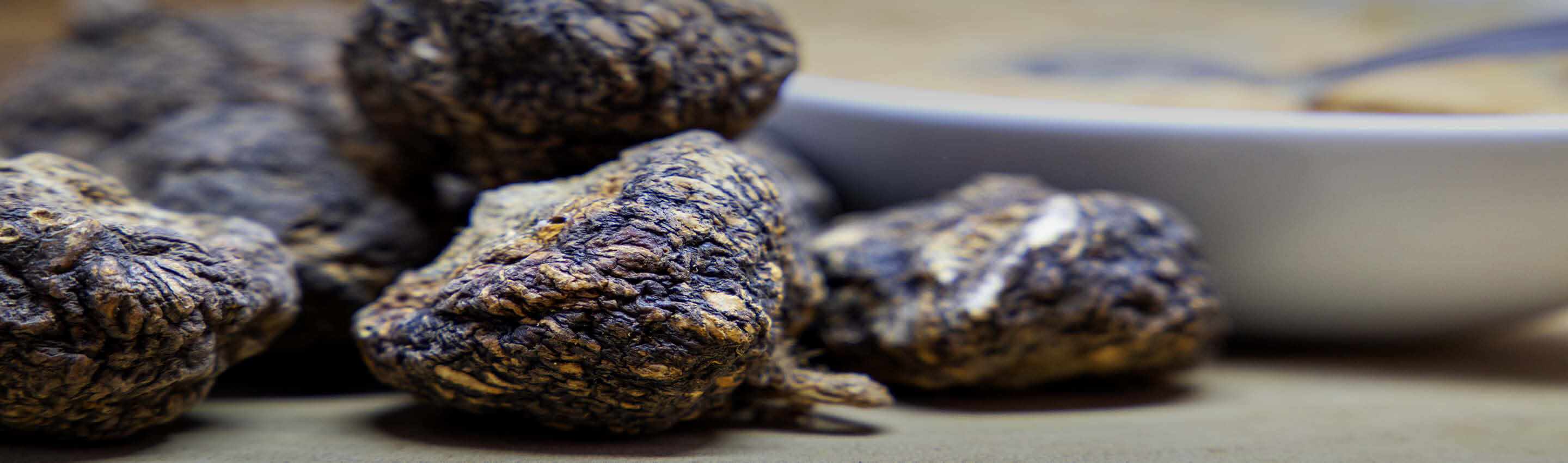 Maca kaufen – traditionell getrocknetes Maca schwarz aus Peru | EDEL KRAUT Getrocknete schwarze Maca-Wurzel vor einer Schale mit Maca-Pulver