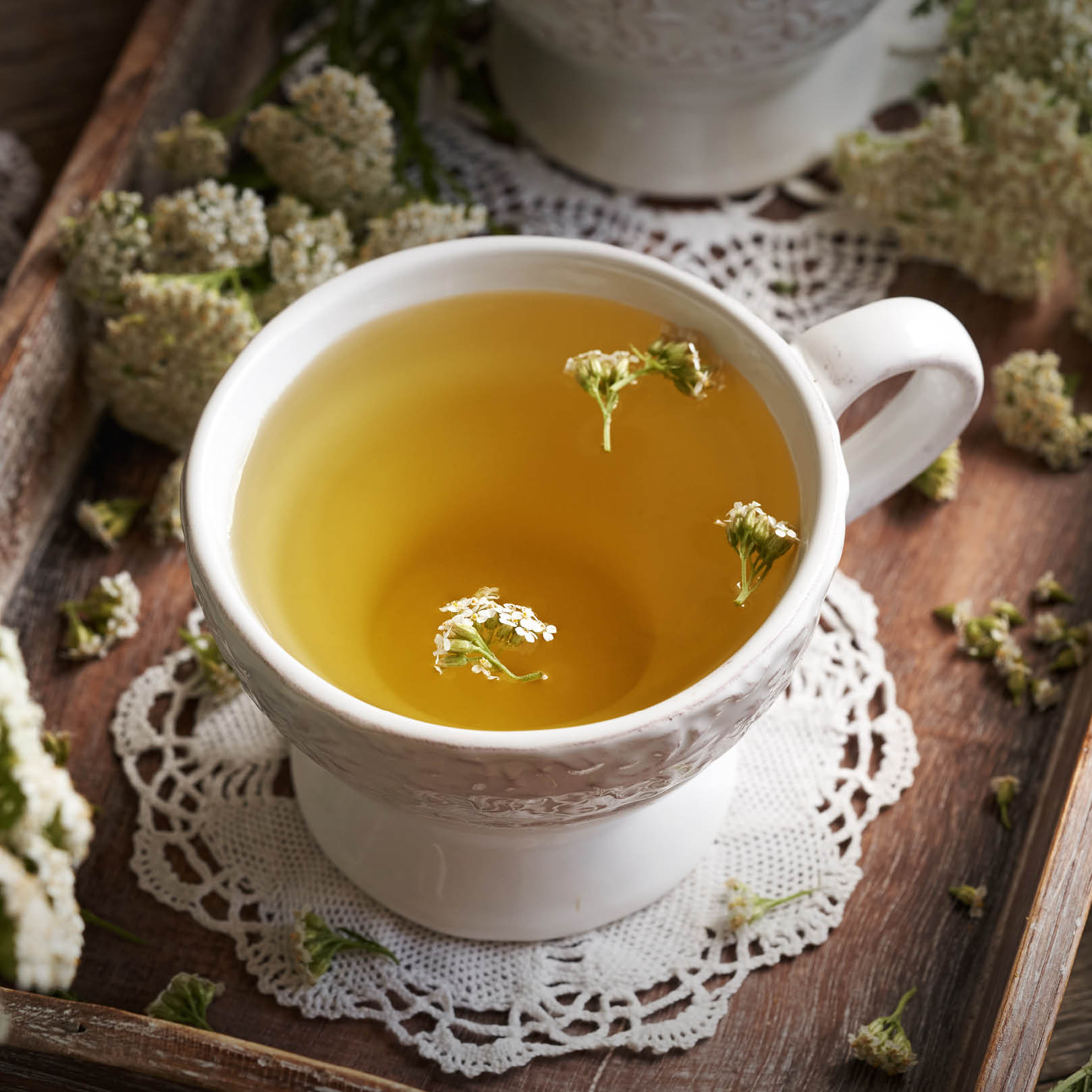 Schafgarben-Tee Bio – traditionell & fein aromatisch Tasse mit zartgelbem Schafgarben-Tee und Blütendekor auf Holztablett